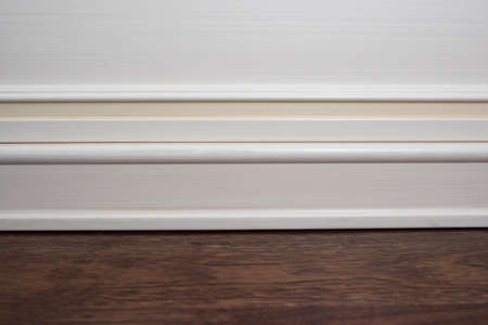 Matte wall, white baseboard and tiles immitating hardwood flooring.