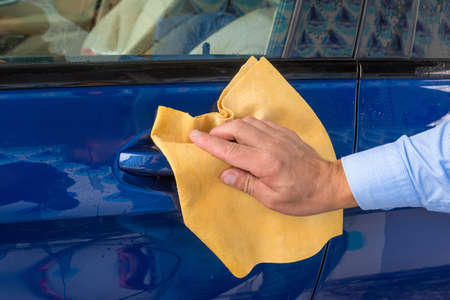 The hand of man wipes a car a yellow rag.の写真素材