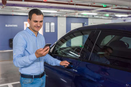 Young man with phone opening blue car door.の写真素材