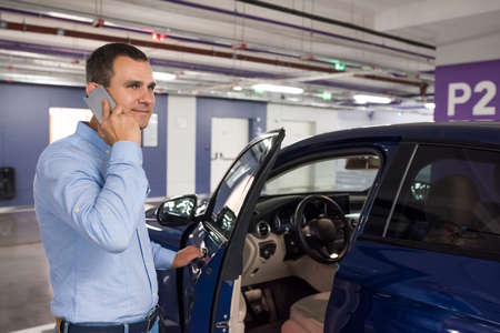 Young man with phone opening blue car door.の写真素材