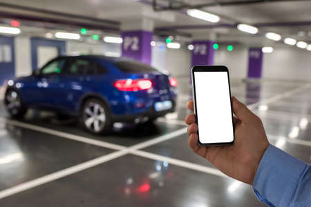Smart phone with white screen in hand on car parking background.の写真素材