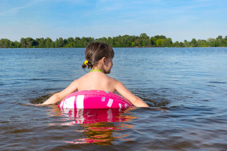 A happy little girl on an inflatable pink circle in the water. A view from the back.の写真素材