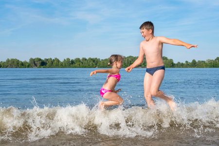 Children play with splashes of water on the river bank. Golden time. Beach season.の写真素材