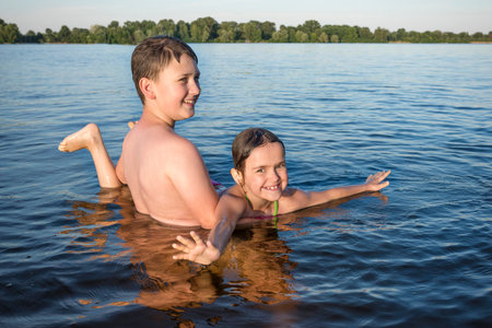 A boy and a girl play in the river, holding her in their arms. A close-up.の写真素材