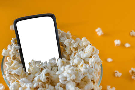 Mobile phone and popcorn in a bowl, on a yellow table, close-up. Technology concept.の写真素材