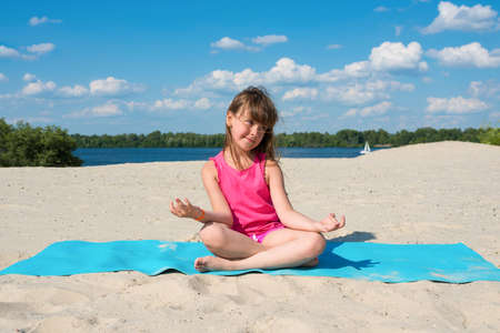 Little girl doing gymnastic exercises while relaxing on the beach on a sunny warm summer day. Concept about sports and active games in summer. Healthy lifestyleの写真素材