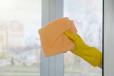 A female hand in a yellow glove wipes a dirty window. House cleaning. Household concept