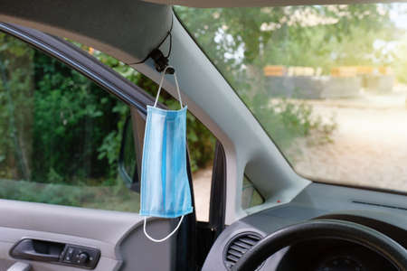 The medical mask hangs on the rearview mirror inside the car. Coronavirus Covid-19. Pandemicの写真素材
