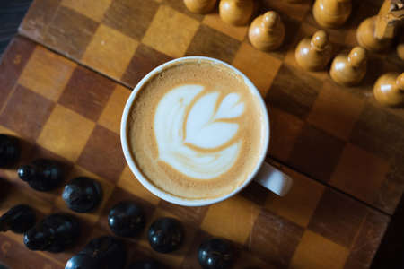 Cup of coffee and chess-board by close-up on a wooden background. Kind from above. Cappuccinoの写真素材