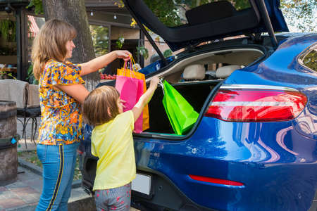 A mother with a little daughter are putting their luggage in a car trunk.の写真素材