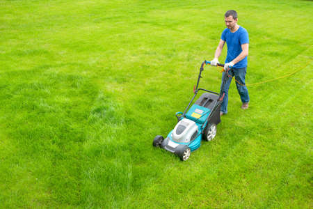 A gardener with a lawn mower is cutting grass in the park. A view from above. A worker is cleaning...