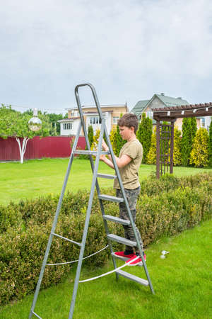 A boy on a ladder is cleaning in the backyard. Garden care.の写真素材