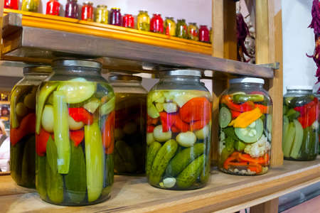 Preservation stands on a counter. Pickled vegetables in a bank, cucumbers, pepper.