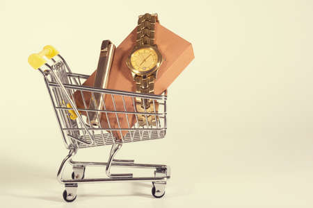 A golden watch in a shopping cart at the white background. Presents, purchases. A toned photo