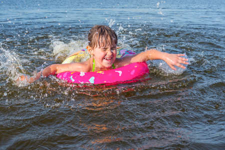 Happy little girl plays in the pool on a pink rubber ring.