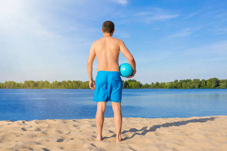 A man with a volleyball ball on the beach on a sunny day. The view from the back.の写真素材