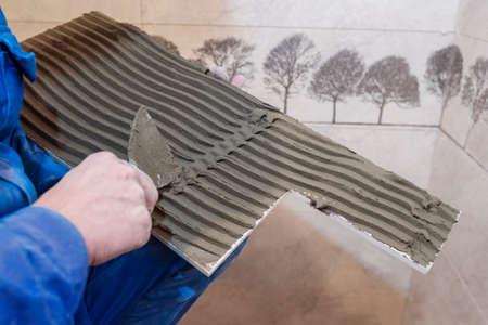 The builder applies an adhesive base to ceramic tiles. The process of laying floor tiles.