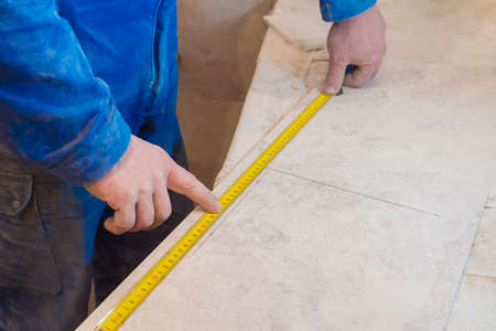 Builder with a measuring tape measures the tiles. Construction repair work in the room for laying ceramic tiles.の写真素材