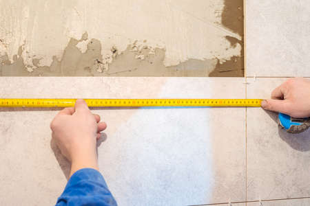 Workers hands and measuring tape. Construction repair work in the room for laying ceramic tiles.