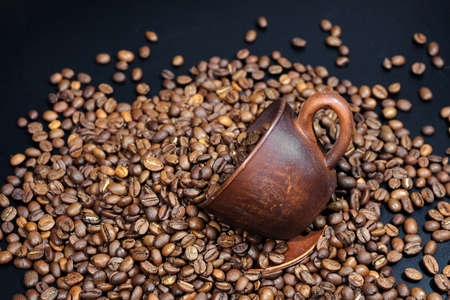 Scattered roasted coffee beans and coffee cup on a black background.