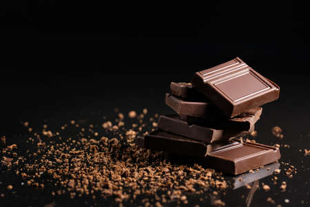 Broken pieces of chocolate with cocoa powder on a black background.の写真素材