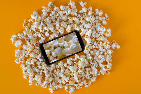 Smartphone and popcorn on yellow table. Technology concept. cinema on a smartphone with background...