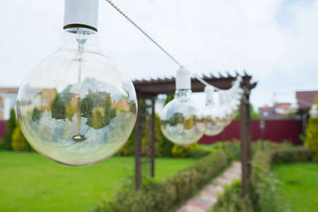 A close-up of an incandescent lamp hanging in the garden backyard.