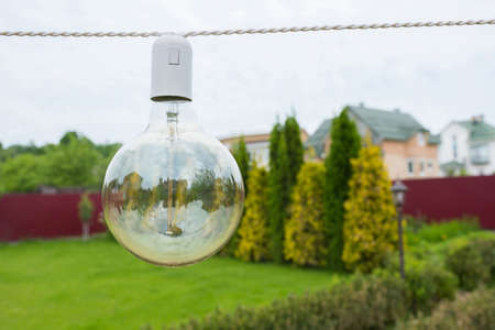 A close-up of an incandescent lamp hanging in the street in the daytime, in the garden backyard.の写真素材