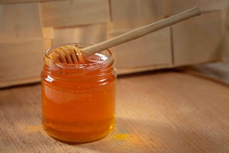 Liquid honey with a honey dipper in a glass jar on a wooden table. Healthy organic honey.の写真素材