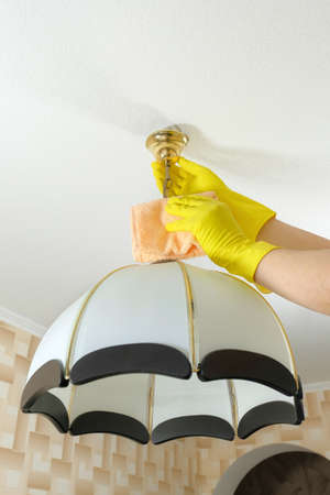 A cleaner in rubber gloves and a cloth wipes the dust from the chandelier. House cleaning.
