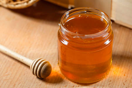 A jar of fresh honey and a honey ladle on a wooden table.の写真素材