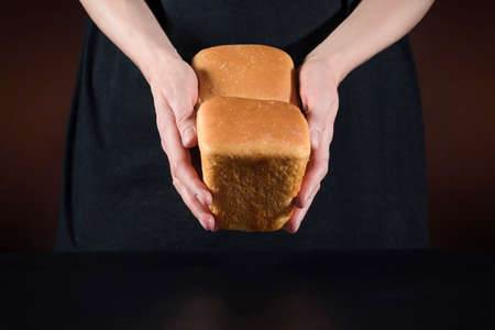 Homemade bread in the female hands of a chef on a dark background.