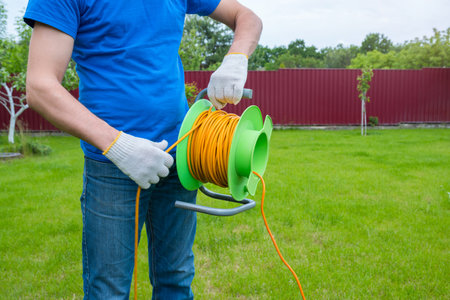 An electrician is unrolling an extension cord on the coil in the house backyard. Cleaning of the...
