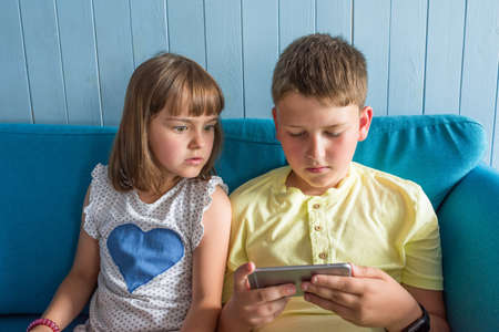 Girl and boy are sitting on the couch with a smartphone. The concepts of children's friendship.
