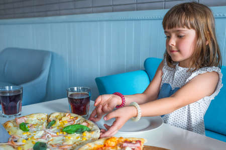 A child in a cafe at the table with a pizza and a glass of soda.の写真素材