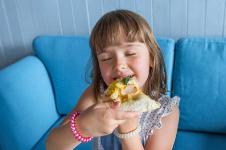 Cute little girl eats pizza. Child has lunch in a cafe, close-up.の写真素材
