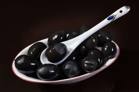 Plate a close up of black olives on a dark red background. Top viewの写真素材