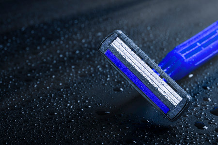 New razor blade with drops of water on a black background. Skin care concept.