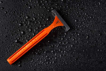 Disposable razor with drops of water on a black background. Skin care concept.の写真素材