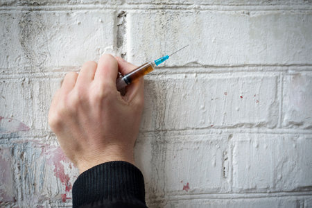 Filled syringe in human hands on a background of a white brick wall. Addiction concept.の写真素材