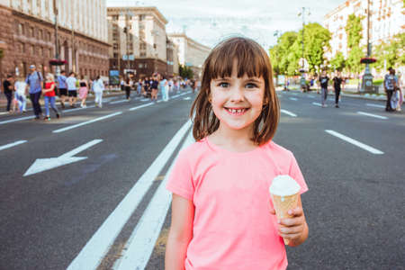 Portrait of a happy child with ice cream in hands on a city street.