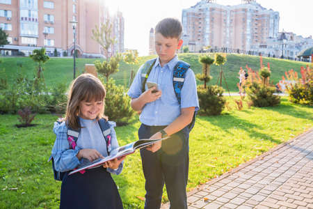 Education, childhood and people concept - happy schoolchildren or brother and sister reading a book...