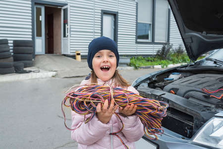 A little girl with a wire in her hands works in the garage. Car service.