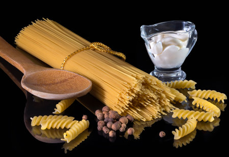 Yellow Italian pasta, spaghetti, black pepper isolated against the black isolated background. A beautiful still life. A close-up.の写真素材