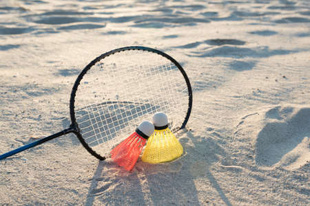 The concept of sports games and summer recreation. Beach badminton. Racket and two shuttlecocks on the sand at sunset.の写真素材