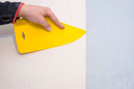 Worker smoothes the wallpaper with a plastic yellow spatula.