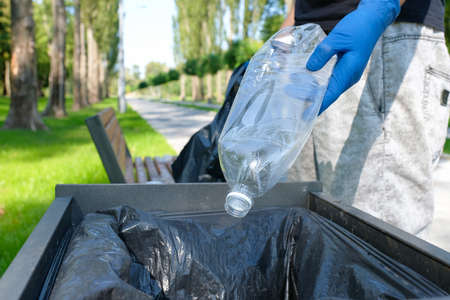 A plastic bottle in the hand of a volunteer picking up rubbish in a public park and throwing the bottle into the trash can. Environmental protection conce.の写真素材
