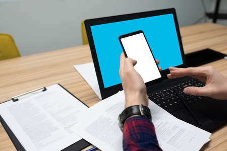 Blank screen phone mockup image with white background. Young businessman working in the office with the phone and computer at the office table.の写真素材