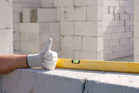 Worker hand showing thumb up, on a construction site. Building a house from a gas block or foam block. Construction and renovation concept.の写真素材