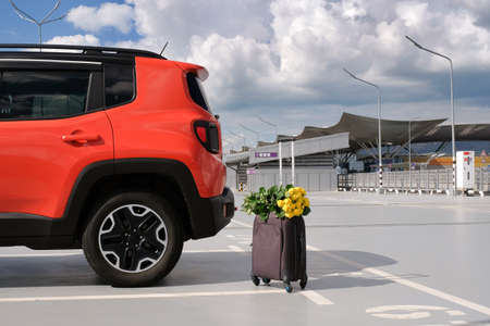 Family orange car, suitcase and a bouquet of flowers in an empty airport parking lot. Summer vacation concept.の写真素材